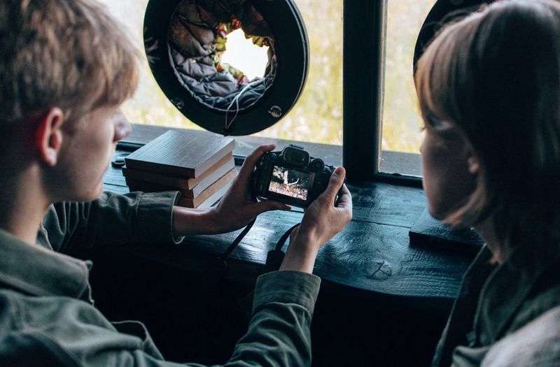 Two young people in a darkened bird hide study an image of a kestrel in flight on a camera touchscreen.