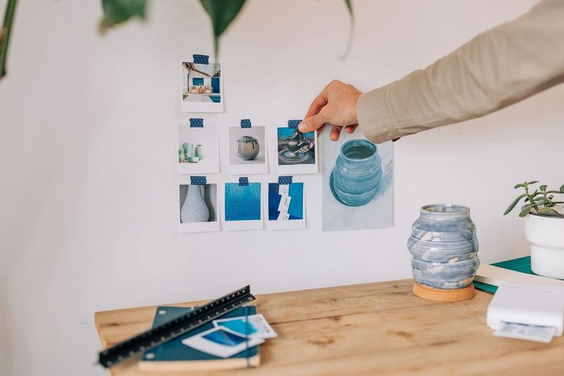 A person making a blue-themed mood board with images stuck on a white wall behind a desk.