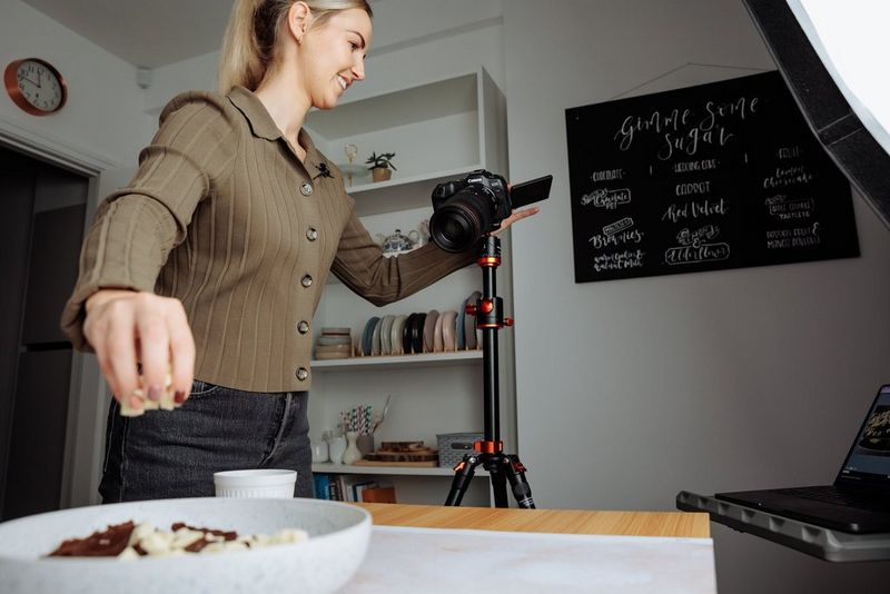 A woman aims her Canon EOS R8 towards a bowl of different types of chocolate as she sprinkles white chocolate chunks on top.
