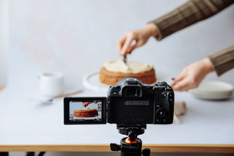 A Canon EOS R8 set up to film a hand swirling frosting on the top of a cake.