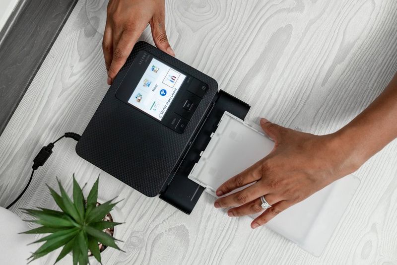 A pair of hands loads a cartridge into the Canon SELPHY CP1500.