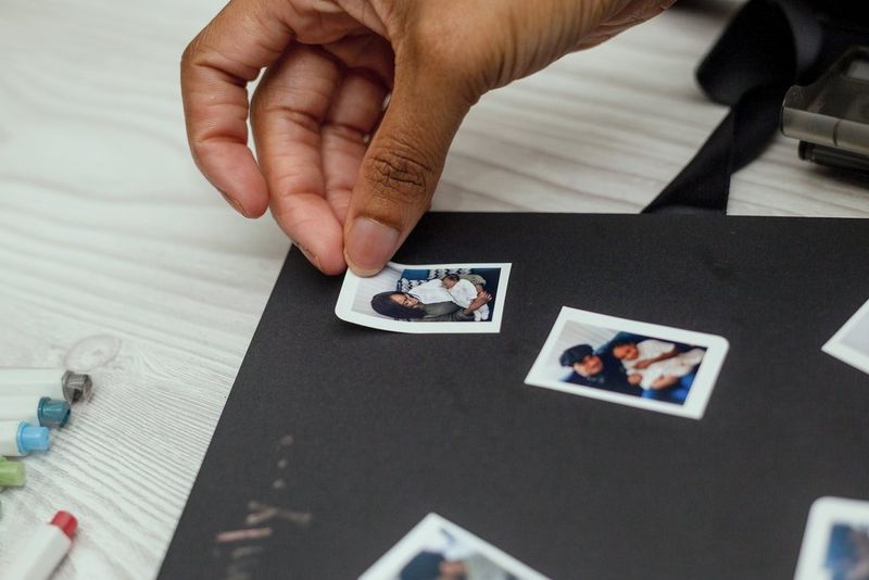 A person sticks a printed photo of a mother holding a baby in their scrapbook.
