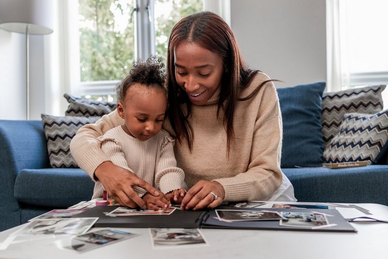 A person helps her child to stick photos in a scrapbook by guiding the child's hands.