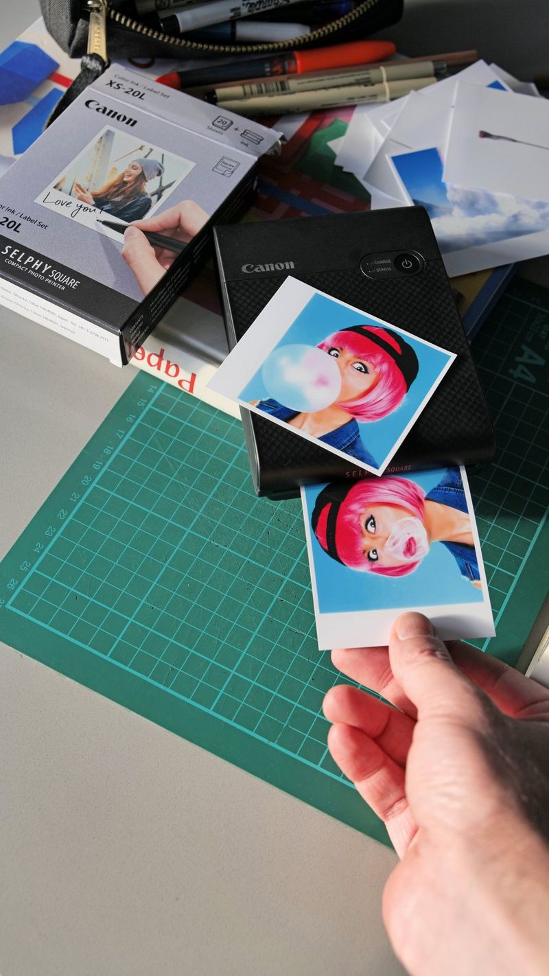 A Canon SELPHY Square QX10 prints a colourful illustration of a young girl with pink hair and bubblegum on her face.