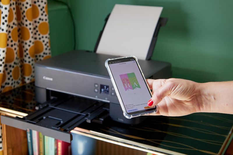 A hand holds a smartphone with the screen displaying a template from Creative Park while a Canon PIXMA printer sits on a table. 