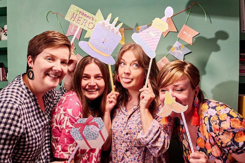 Four people smile as they pose with papercraft photo booth props created using Canon Creative Park and a PIXMA printer.