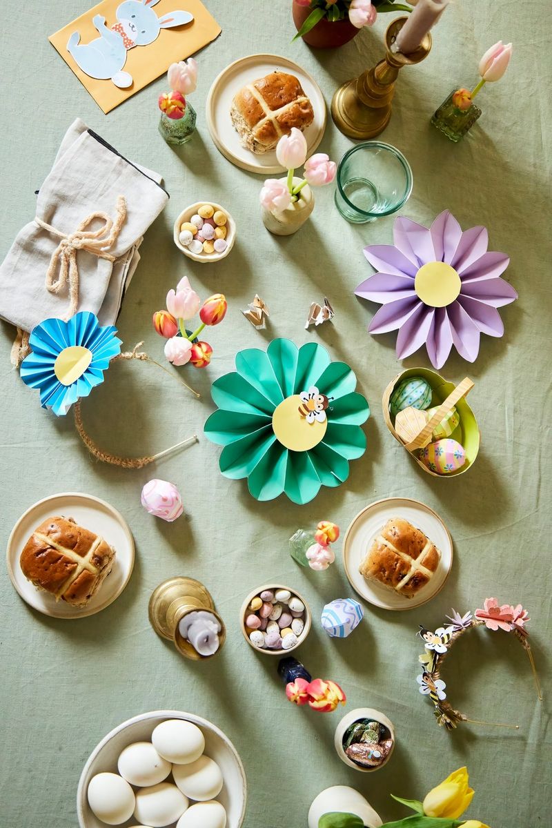 A table covered with Creative Park papercraft decorations, flowers in vases and several plates of food including eggs and hot cross buns.