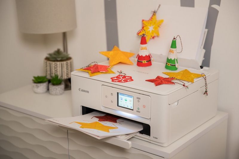 A Canon PIXMA printer sits on a small sideboard, covered in a selection of papercraft Christmas decorations and with a Creative Park template in the printer tray.