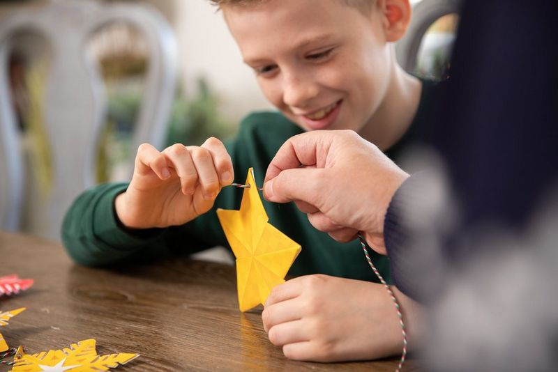 Chris helps his son thread twine through a hole in the top of his papercraft star decoration.