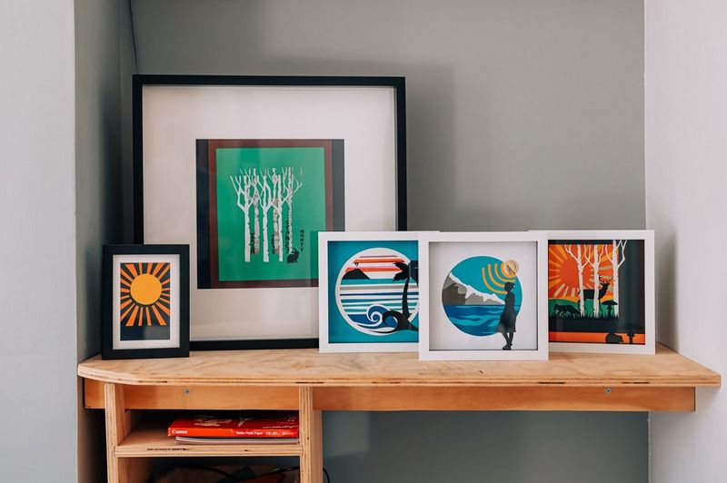 A row of framed papercraft art pieces of different sizes standing on a desk.