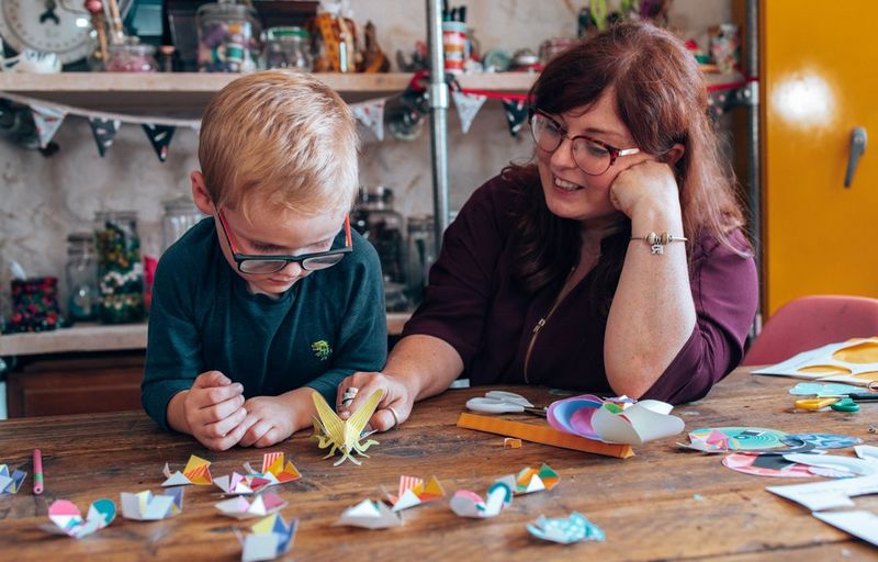A smiling woman and a young boy sitting at a table playing with a selection of papercraft fidget toys.