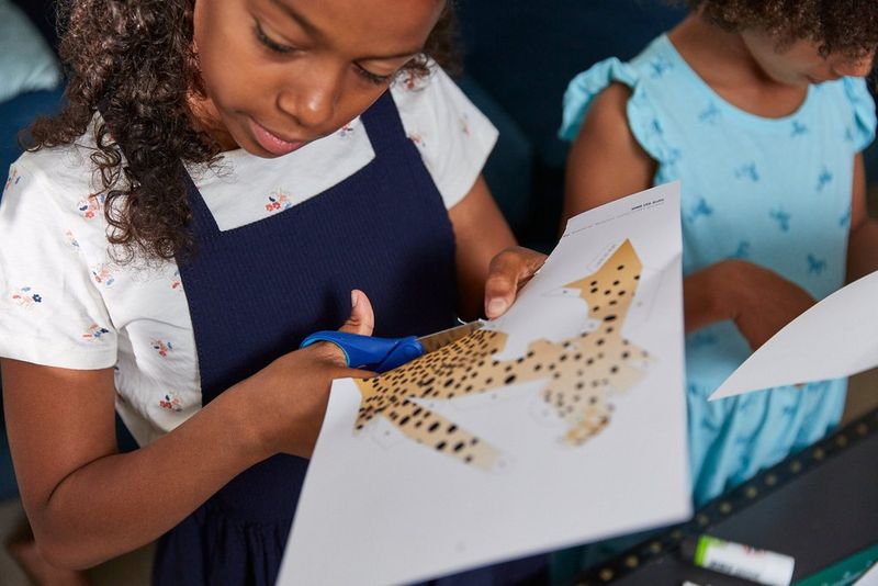 A girl cutting out a cheetah-spotted shape printed on A4 paper.
