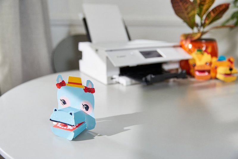 A paper hippopotamus hand puppet on a round table next to a Canon PIXMA printer.