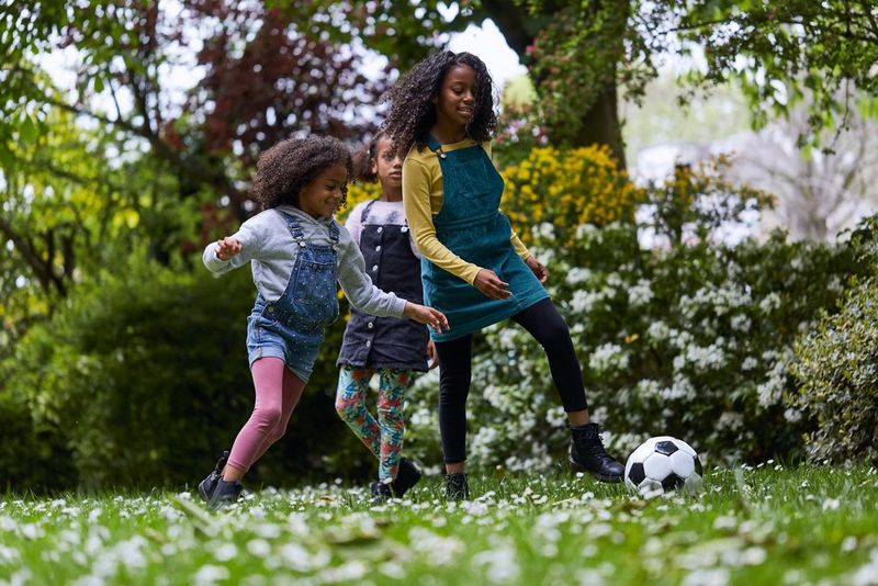 Three young girls kicking a football around their garden.
