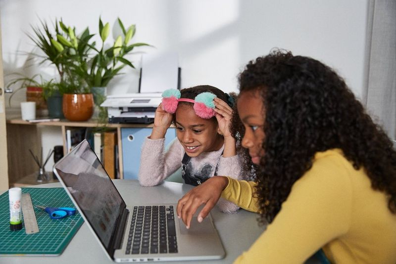 Two girls sitting at a table using a laptop.
