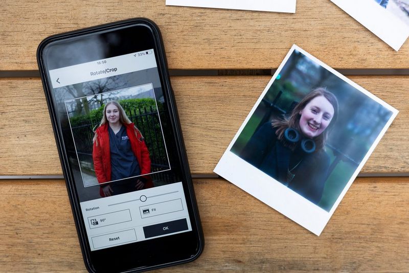 A smartphone showing the SELPHY Photo Layout app and a printed portrait photo are laid out on a wooden table, shot from above.