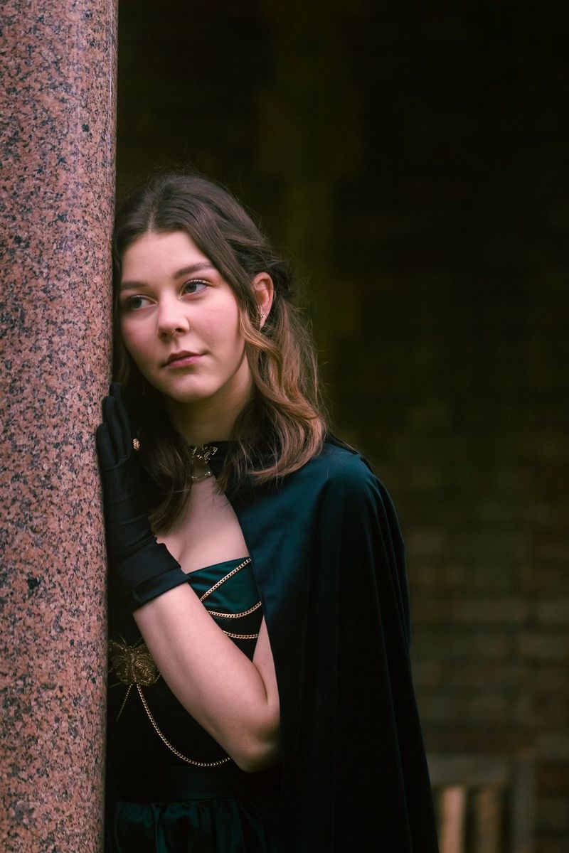 A figure dressed as a princess leans against a wall looking wistful at a renaissance fair.