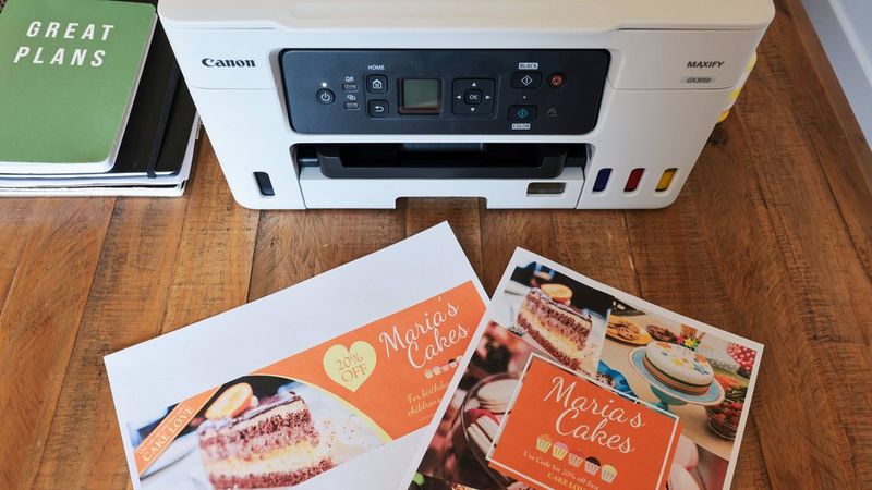 Printed Canon PosterArtist designs on a desk in front of a Canon MAXIFY printer. 