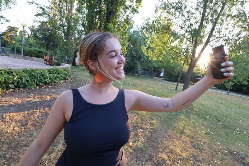 Travel and lifestyle vlogger Celia Castle stands in a park and smiles into a Canon PowerShot V10, which she holds out in front of her.