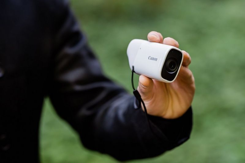 A person holding a Canon PowerShot ZOOM camera.