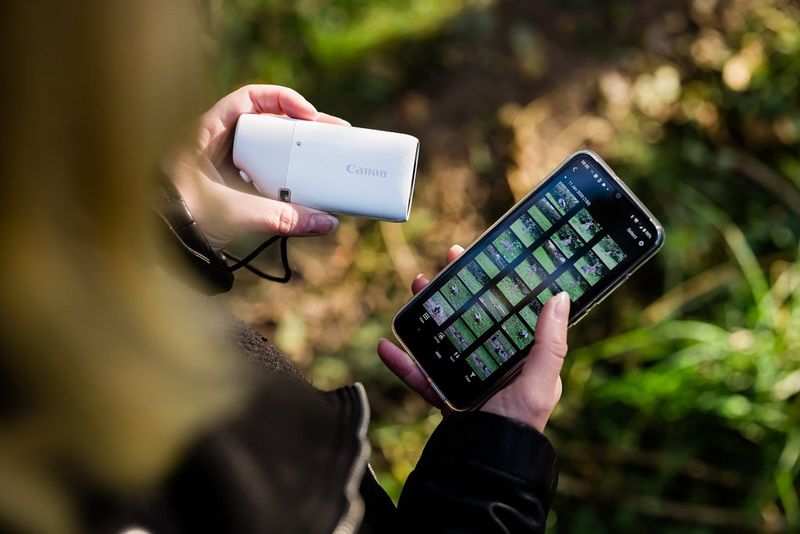 A woman holds a Canon PowerShot ZOOM and connects wirelessly to her smartphone.