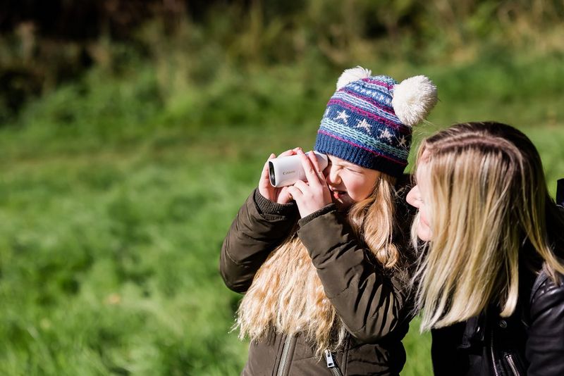 A young girl in a festive woollen hat looking holding a Canon PowerShot ZOOM to her eye.