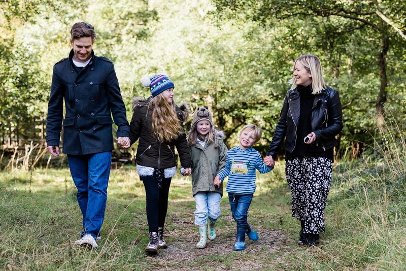 A family of two adults and three children holding hands while walking through the woods on a crisp autumn day.
