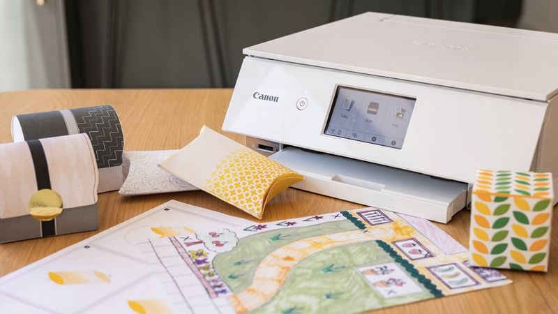 A Canon PIXMA printer on a tabletop with folder paper boxes and a hand-drawn map.