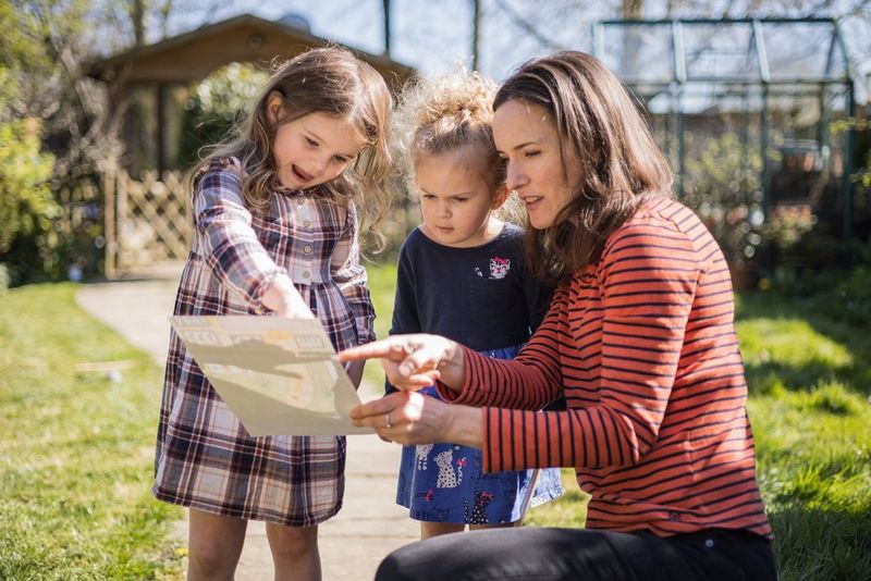 A mother and her young daughters looking at a treasure map in a large garden.