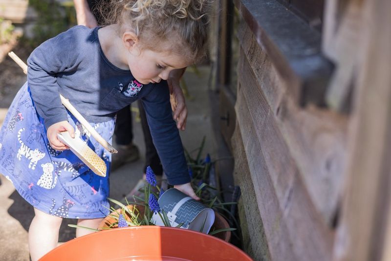 A young girl reaching into a plant pot to pick up a paper treasure chest.