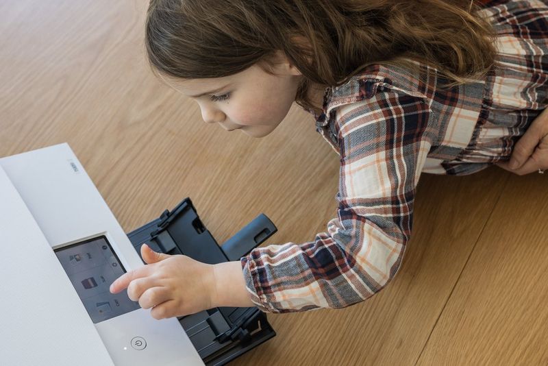 A young girl leaning over a table to press the buttons on the touchscreen panel of a PIXMA printer.