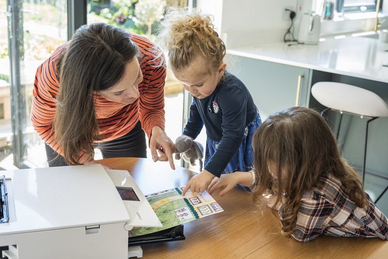 A mother showing her young daughters the map they coloured in being printed out.
