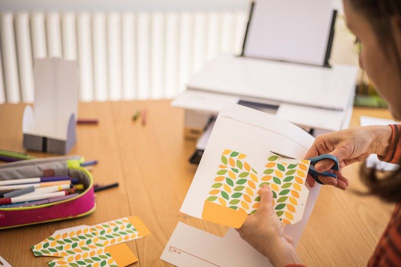 A person cutting out a leaf box design with a pair of scissors.