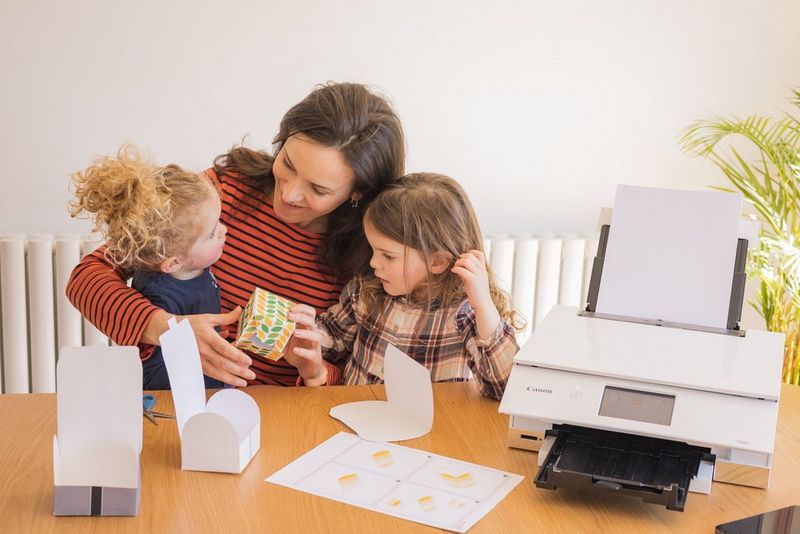 A mother and her young daughters folding and gluing some papercraft boxes.