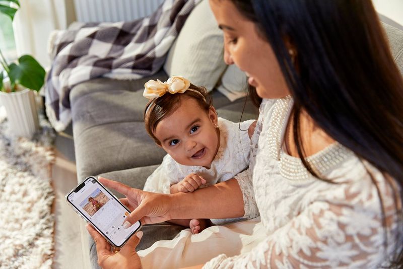 A woman sitting on a sofa with an infant, using the Canon Easy-PhotoPrint Editor app on her phone to edit a photo calendar.   