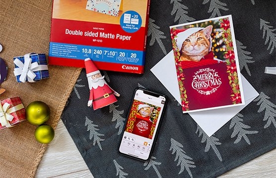 A home-printed Christmas card alongside crafted decorations and Canon Double-sided Matte Paper arranged on a cloth with a Christmas tree motif.