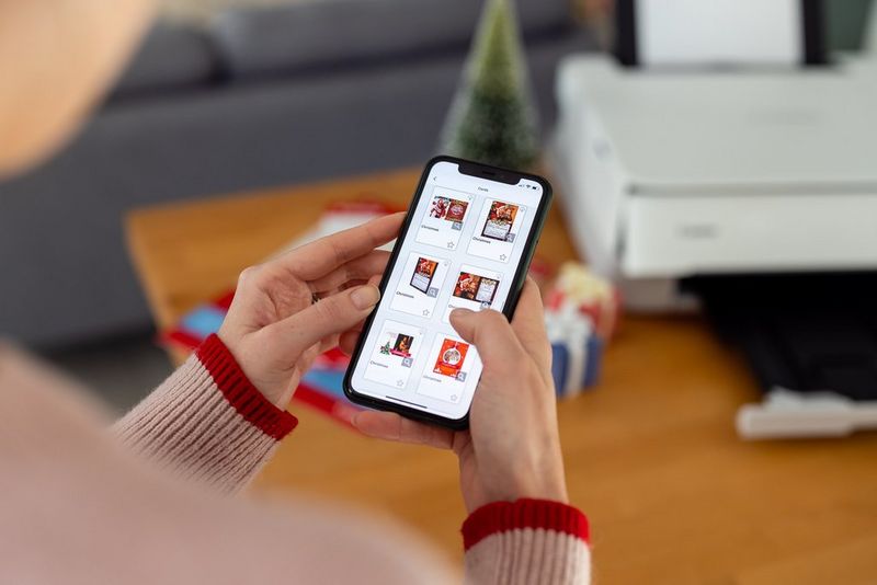 A woman scrolls through the Christmas card templates in the Easy-PhotoPrint Editor app on her smartphone.