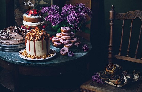 A low-light shot, featuring a table of cakes and flowers. 
