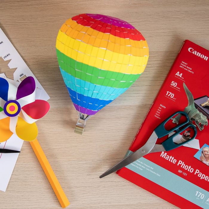 A flat lay image of a wooden desk with a colourful papercrafted windmill and hot air balloon, plus a pack of Canon photo paper.  