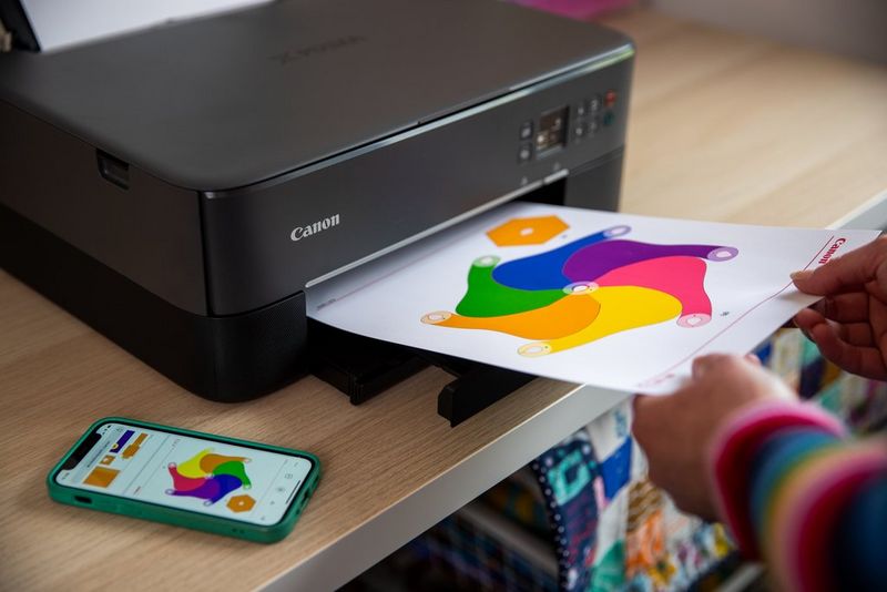 A piece of paper with a template of a colourful windmill on it emerges from a Canon PIXMA printer, which is positioned on a wooden desk.