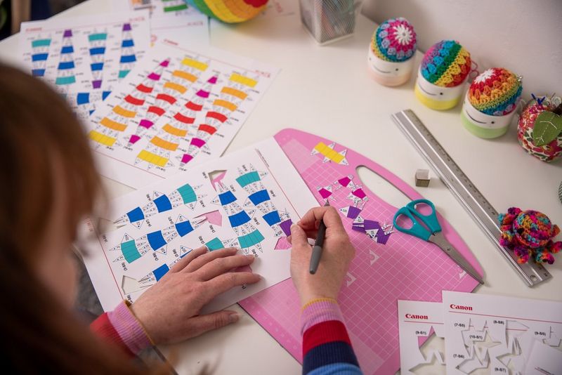 A person leans over a desk to cut out an intricate template using a craft knife. 