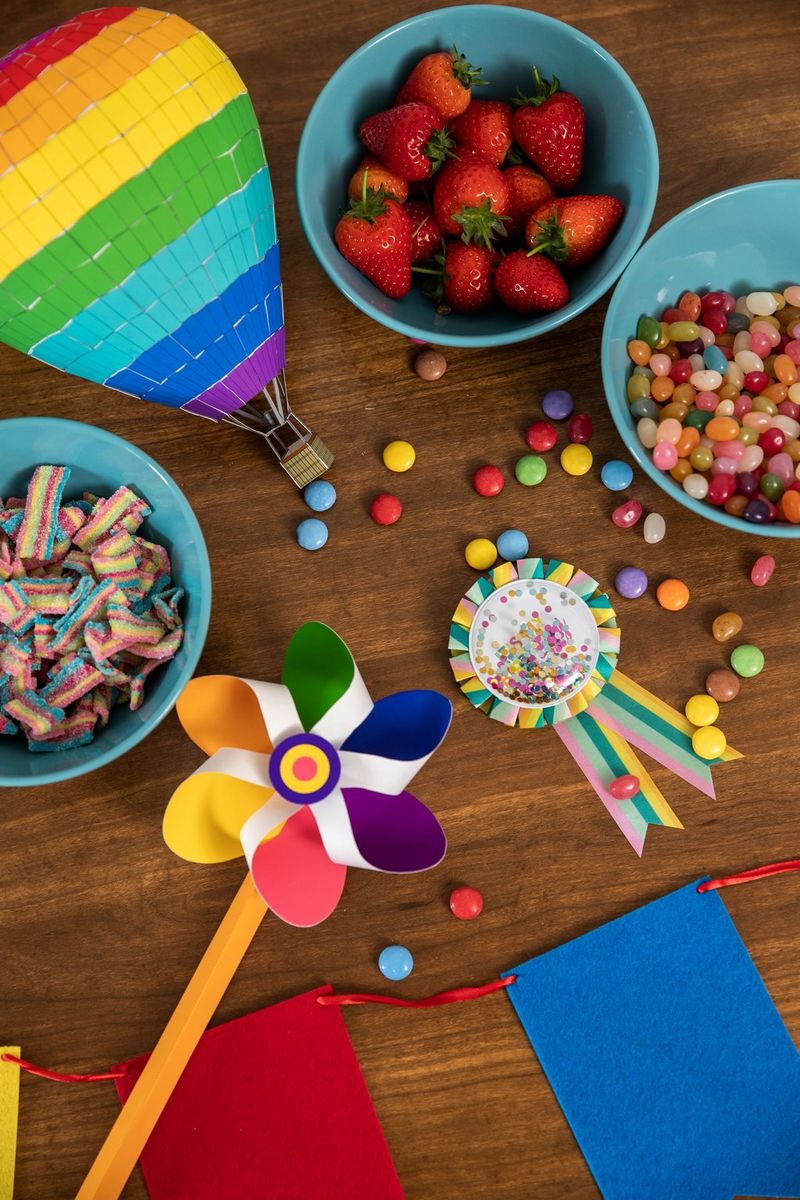 A flat lay image of a wooden desk with a colourful papercrafted windmill and hot air balloon, plus several bowls of sweets and fruit. 