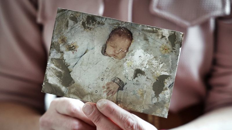 Hands holding a damaged photograph of a sleeping baby.