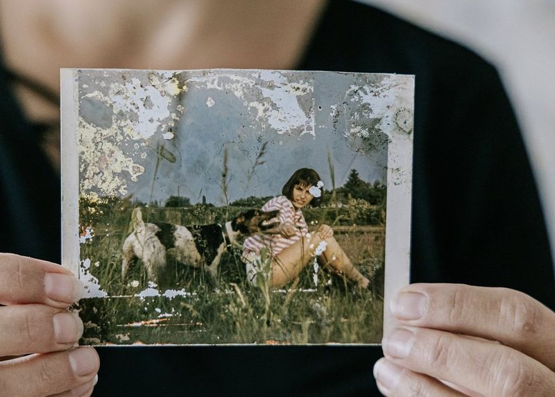 A flood-damaged photo of a young woman sat amongst grass with a dog.