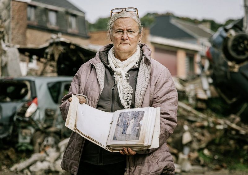 A woman standing amidst debris holding a photo album containing a damaged wedding photo.