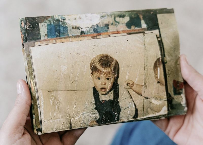 Hands holding up a sheath of damaged photographs, the topmost a portrait shot of a young child.