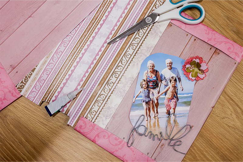 A picture of a girl and a boy on the beach with their grandparents. Underneath it and next to it are different patterned papers and a handcrafted flower, all in shades of pink.