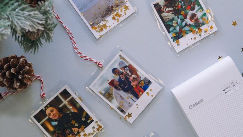 A flatlay of a selection of Christmas photo decorations alongside a Canon SELPHY Square QX10 printer.