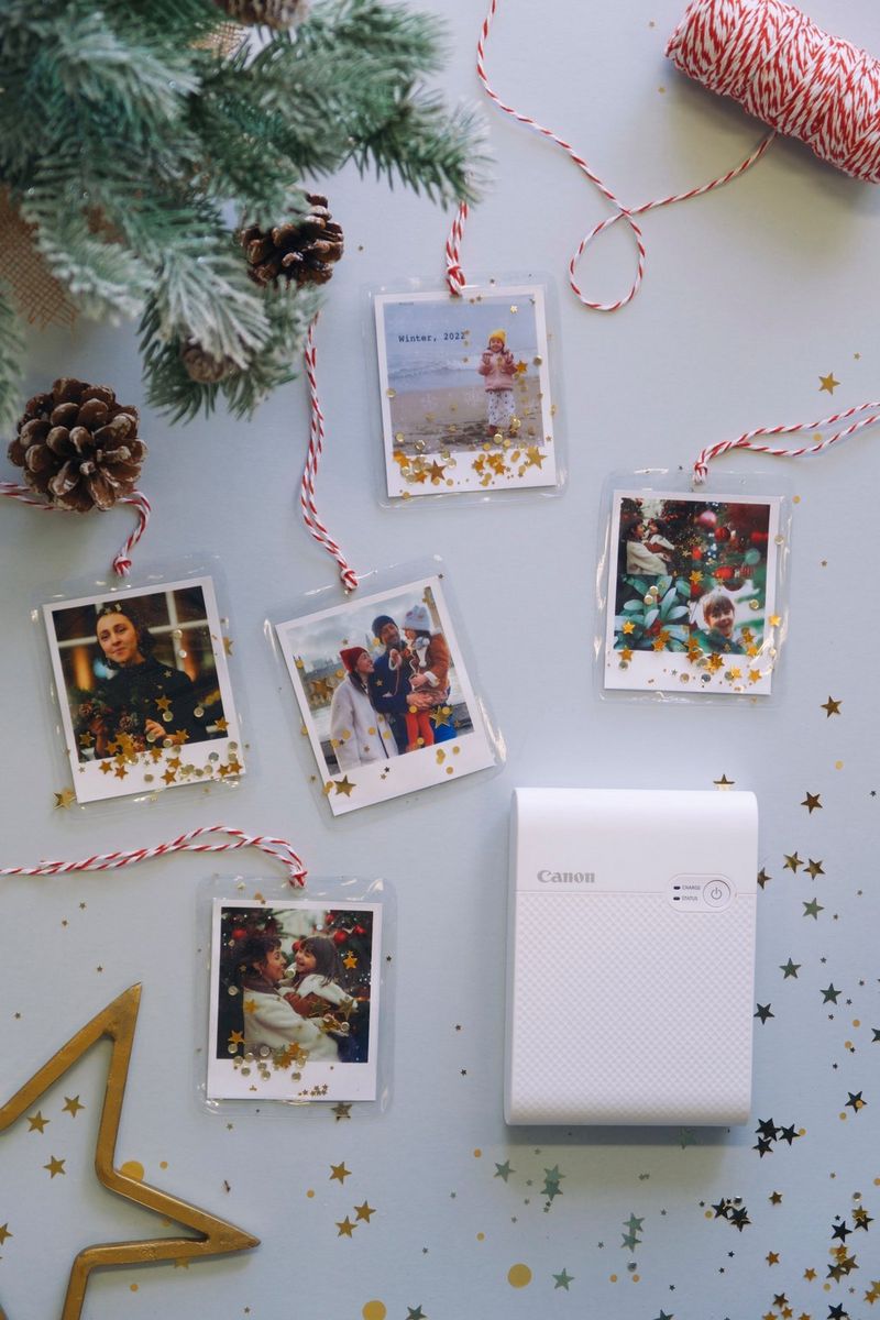 A flatlay of a selection of Christmas photo decorations plus a Canon SELPHY Square QX10 printer, sequins and festive accessories.