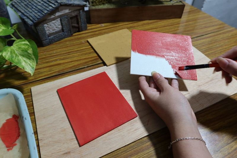 A pair of hands paint two pieces of hard foam red in order to construct the gallery walls.
